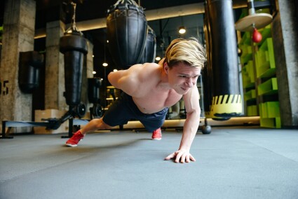 Athletic man which doing push-ups on one hand in gym