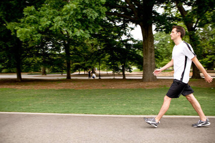 A young caucasian man exercising in the park by speed walking. Panning technique used for intentional blurring of background to emphasize motion.