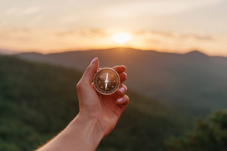 Explorer young woman holding compass in hand in summer mountains at sunrise, point of view. Concept of hiking and travel. (Explorer young woman holding compass in hand in summer mountains at sunrise, point of view. Concept of hiking and travel., ASCII